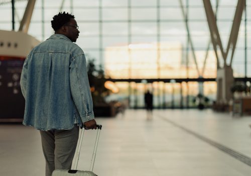 A man pulling a suitcase walks through a well-lit and modern airport terminal, suggesting travel, exploration, or jet-setting lifestyle moments, capturing a contemporary and stylish ambiance.
